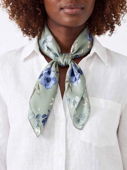 Silk neck scarf with light blue and green floral pattern, tied knot close-up